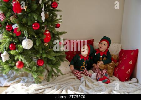 Mädchen und Kleinkind, gekleidet als Elfe, sitzen vor dem Weihnachtsbaum Stockfoto