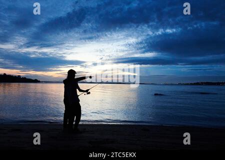 Silhouette von Vater und Sohn beim Angeln am Strand bei Sonnenaufgang Stockfoto