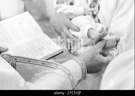 Der Priester führt den Ritus der Taufe des Kindes aus und salbt das Bein mit heiliger Myrrhe, dem Sakrament der christlichen Taufe. Stockfoto