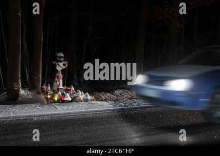 Das Kreuz mit Motorradhelm am Straßenrand und vorbeifahrendem Auto bei Nacht Stockfoto