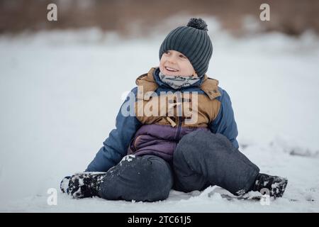 6-jähriger Junge lächelt und sitzt auf Schnee. Stockfoto