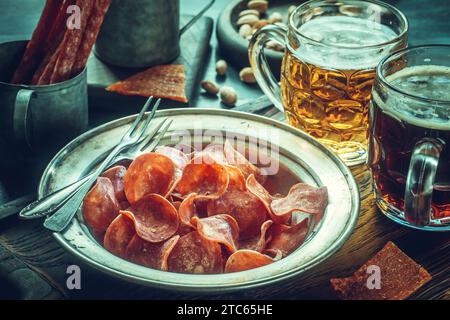 Jerky Schweinefleisch-Chips auf Vintage-Teller mit Bier auf dem Tisch. Getrocknete Fleischscheibe Stockfoto