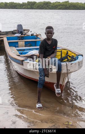 Junge, der auf dem Bug eines Bootes sitzt, das am Ufer des Saloum Delta im Senegal gestrandet ist Stockfoto