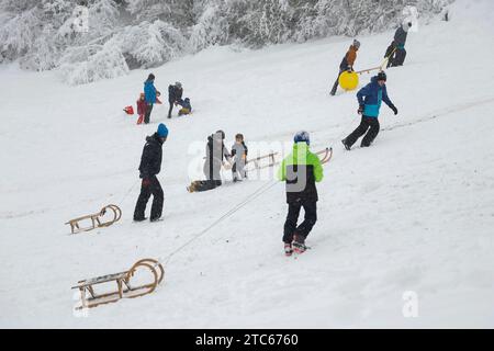 Leute mit Schlitten, die auf einem schneebedeckten Hügel in München, Bayern, Deutschland klettern. Stockfoto