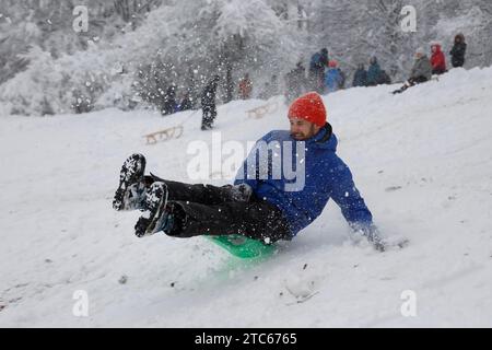 Mann, der einen schneebedeckten Hügel hinunterfährt, der durch die Luft fliegt in München, Bayern, Deutschland, Stockfoto