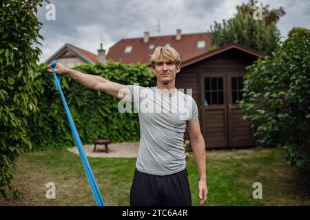 Mann mittleren Alters, der im Garten Kraftübungen mit Widerstandsband macht. Konzept der Trainingsroutine zu Hause. Stockfoto