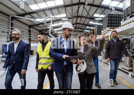 Vollständiges Team von Lagermitarbeitern, die das Lager betreten. Team von Arbeitern, Managern, weibliche Direktorin in modernen Industriefabriken, Schwerindustrie Stockfoto
