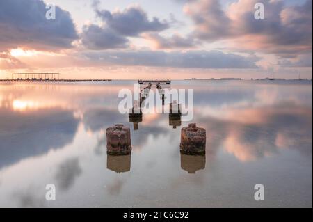 Pfosten von einem ruinierten Steg, die sich bei Sonnenaufgang in ein ruhiges Meer erstrecken. Stockfoto