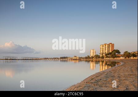 Hochhaus, entlang eines spanischen Strandes, das sich bei Sonnenaufgang im ruhigen Meer spiegelt Stockfoto