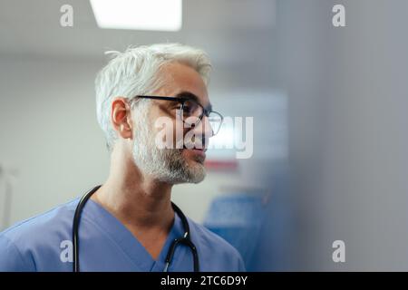 Porträt eines selbstbewussten Reifearztes im Krankenhauszimmer. Schöner Arzt mit grauen Haaren, der medizinische Peelings und Stethoskop um den Hals trägt Stockfoto