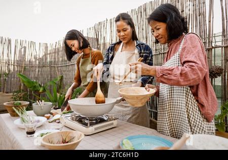 Südostasiatische Mutter und ihre Töchter haben Spaß dabei, gemeinsam auf der Terrasse des Hauses thailändische Gerichte zuzubereiten Stockfoto