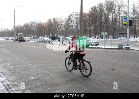 Sankt Petersburg, Russland. Dezember 2023. Ein Kurier auf einem Fahrrad liefert eine Bestellung auf einer verschneiten Straße in St. Petersburg. Quelle: SOPA Images Limited/Alamy Live News Stockfoto