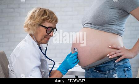 Der Arzt hört dem Herzschlag des Babys einer schwangeren Frau zu. Stockfoto