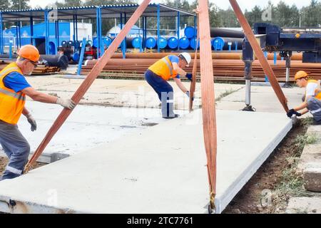 Professionelle Bauarbeiter arbeiten auf der Baustelle. Ein Team von Schleudern legt am Sommertag eine Betonplatte auf den Boden. Echter Workflow. Stockfoto