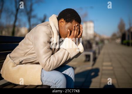 Außenporträt einer depressiven afroamerikanischen Frau am sonnigen Tag. Sie sitzt auf einer Bank auf der Straße. Stockfoto
