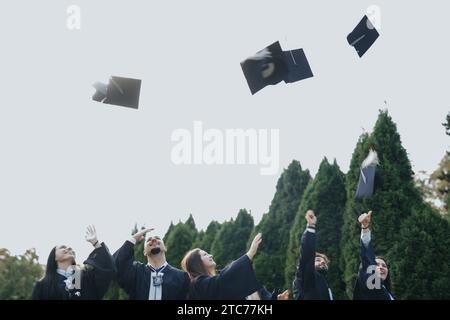 Joyful University-Absolventen feiern den Erfolg im Sunny Park mit einer Zeremonie zum Verwerfen von Kappen Stockfoto