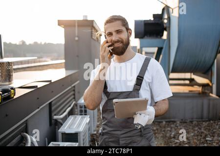 Mann Ingenieur, der auf dem Handy spricht und das Tablet auf dem Dach hält Stockfoto