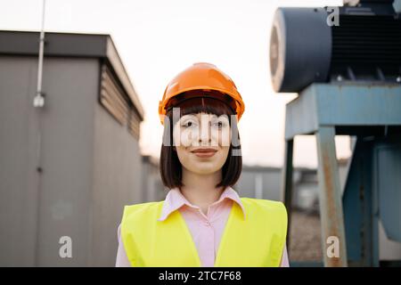 Frau mit Schutzhelm, die in der Nähe von Industriemaschinen steht Stockfoto