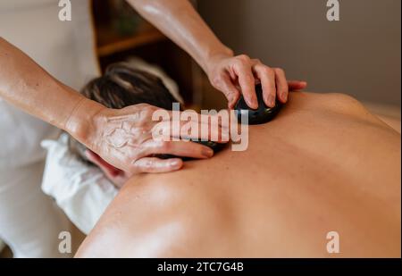 Massagetherapeut verwendet heiße Steine auf dem Rücken des Kunden während einer Spa-Behandlung Stockfoto