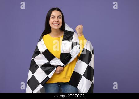 Glückliche junge Frau mit karierter Flagge auf violettem Hintergrund Stockfoto