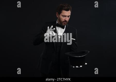 Magier zeigt Zaubertrick mit Hut auf schwarzem Hintergrund Stockfoto