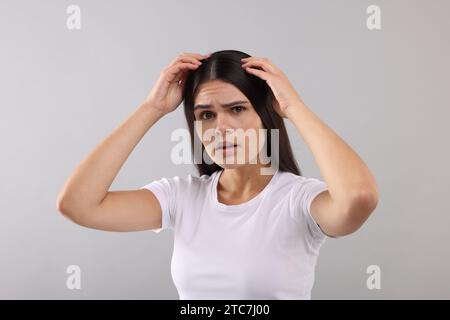 Emotionale Frau, die ihr Haar und ihre Kopfhaut auf grauem Hintergrund untersucht Stockfoto