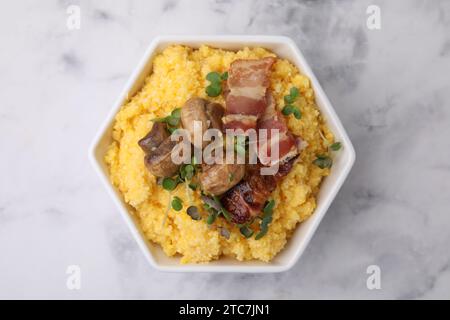 Gekochtes Maismehl mit Speck, Pilzen und Mikrogrün in Schüssel auf weißem Marmortisch, Blick von oben Stockfoto