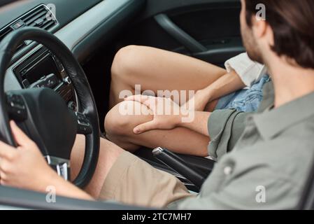 Zugeschnittene Ansicht eines Mannes, der das Bein einer Frau berührt, während er im modernen Auto sitzt, Verführung und Romantik Stockfoto