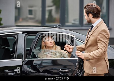 Mann in formeller Kleidung, der Hand einer eleganten blonden Geschäftsfrau hält, die auf der Straße ein Luxusauto verlässt Stockfoto