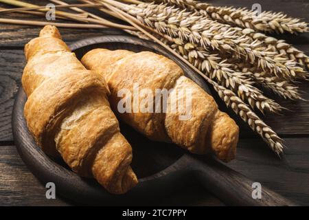 Croissants und Weizenohren auf dunklem Holztisch in Nahaufnahme Stockfoto