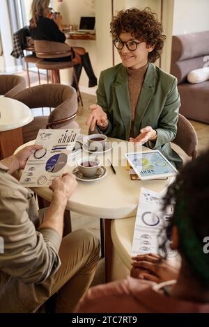 Kaukasische Geschäftsfrau zeigt Dokumente mit Statistiken unbekannten Männern und Frauen in der Cafeteria Stockfoto