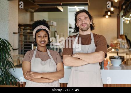 Ein lächelnder kaukasischer Mann und eine fröhliche schwarze Frau stehen zusammen an ihrem Arbeitsplatz in der Cafeteria Stockfoto