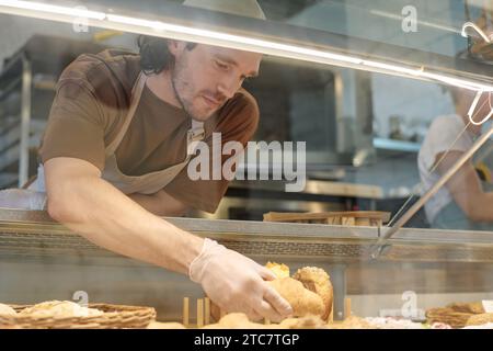 Cafe-Mitarbeiter, der Gebäck in Schaufenster zum Verkauf präsentiert Stockfoto
