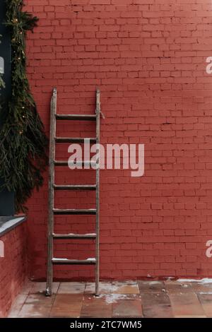 Rote Ziegelwand mit Holzleiter, verziert mit Tannenzweigen. Neujahr und Weihnachten Stockfoto