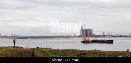 Hartlepool Kernkraftwerk aus Sicht von South Gare, Redcar, England, Großbritannien. Eine Frau beobachtet, wie ein Bagger, Heortnesse, Teesport verlässt. Stockfoto