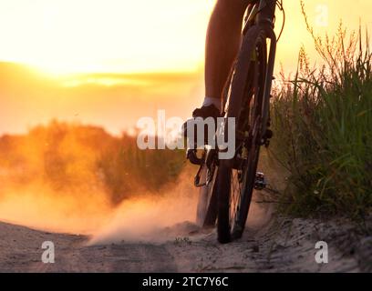 Radfahrer schleudern bei Sonnenuntergang auf einer sandigen Straße auf einem Feld viel Staub vom Hinterrad. Stockfoto