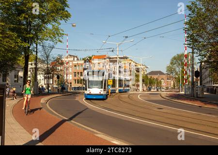 Straßenbahn und Frau auf dem Fahrrad auf einer Straße in Amsterdam, Niederlande Stockfoto