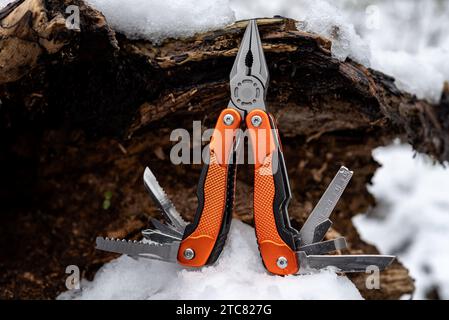 Multifunktionszange mit anderen Werkzeugen und Messer an einem alten, schneebedeckten Hohlbaum. Selektiver Fokus. Stockfoto