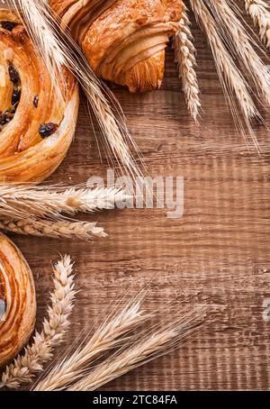 Goldene Weizenohren, Rosinenrollen, Croissant auf Eichenholzplatte, Speisen- und Getränkekonzept Stockfoto