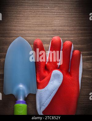 Sicherheitshandschuh und Gartenhandspaten aus Stahl auf Holzoberfläche Stockfoto