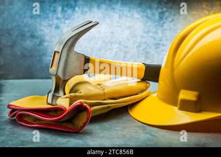 Lederhandschuhe mit Klauenhammer und gelber Helm auf metallischem Hintergrund Stockfoto