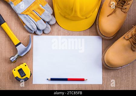 Bleistift und Papier Tapeline Hammer Arbeitsstiefel Helm Handschuhe auf Holzbrett mit Copyspace Stockfoto