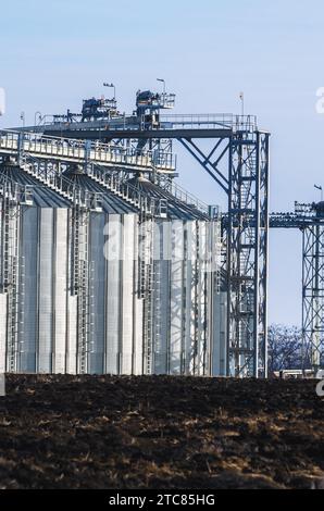 Die komplexen Siloanlagen zur Lagerung von Getreide, die im Winter auf dem gepflügten Feld vor blauem Himmel stehen Stockfoto