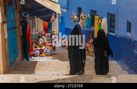 Ein Bild von zwei Frauen, die eine Burka tragen, die in einer Gasse in Chefchaouen laufen Stockfoto