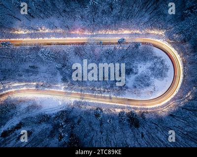 Verschwommene Scheinwerfer vorbeifahrender Autos im Winter nach Einbruch der Dunkelheit. Eisschwarz auf der Straße. Transport im Winter bei Nacht. Stockfoto