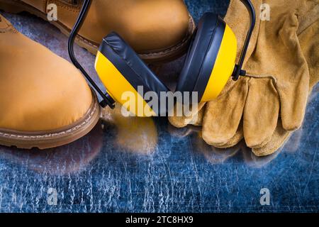 Lederstiefel Schutzhandschuhe und geräuschreduzierende Ohrenschützer auf einem zerkratzten metallischen Hintergrund Stockfoto