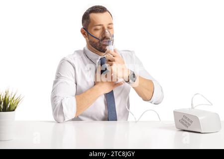 Junger Mann, der an einem Tisch sitzt und einen Vernebler benutzt, der auf weißem Hintergrund isoliert ist Stockfoto