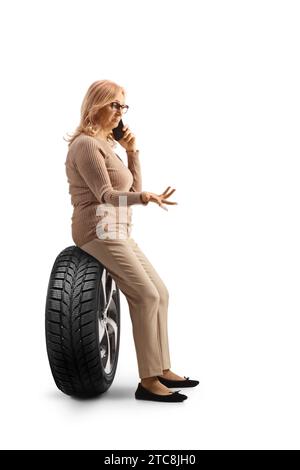 Profilaufnahme einer Frau, die auf einem Autoreifen sitzt und einen Anruf auf weißem Hintergrund tätigt Stockfoto