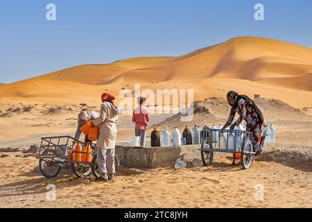 Marokkanische Berberfrauen sammeln Trinkwasser aus Brunnen in Erg Chebbi in der Sahara bei Merzouga, Drâa-Tafilalet, Errachidia, Marokko Stockfoto