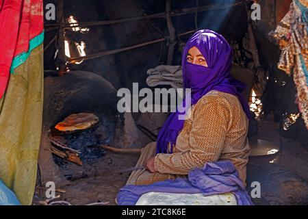 Nomadische Beduinenfrau mit Hijab, die Brot im traditionellen Backofen in der Sahara in der Nähe von Merzouga, Drâa-Tafilalet, Errachidia, Marokko backt Stockfoto